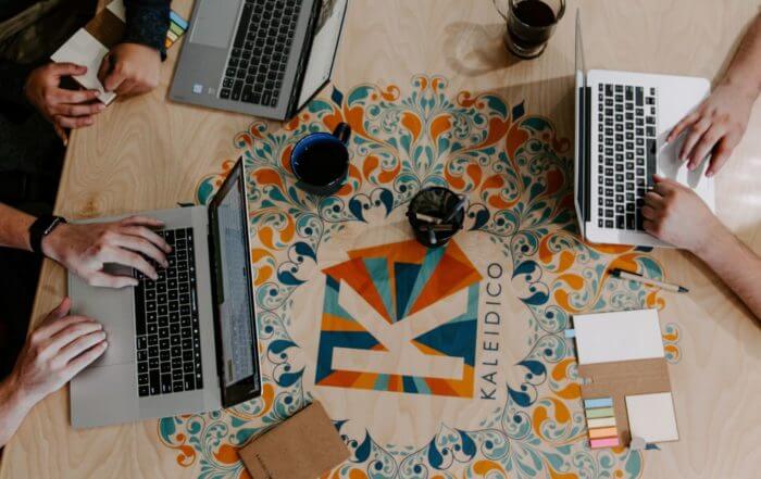 Three people working on laptops around a table with colorful decorative design and cups of coffee.