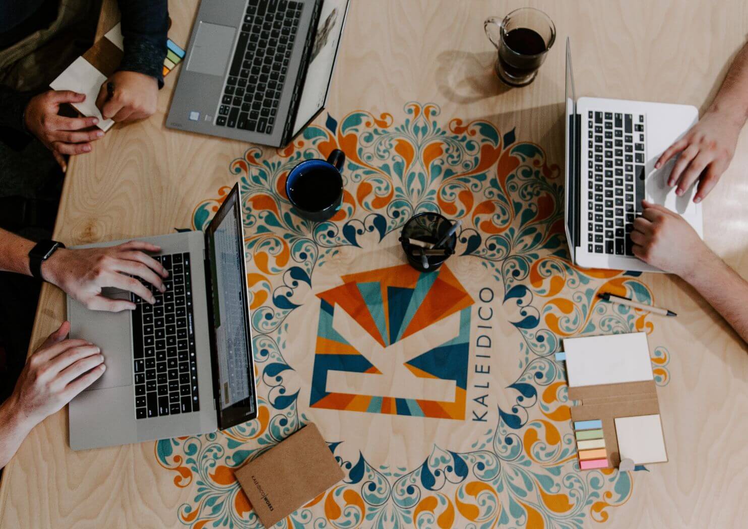 Three people working on laptops around a table with colorful decorative design and cups of coffee.