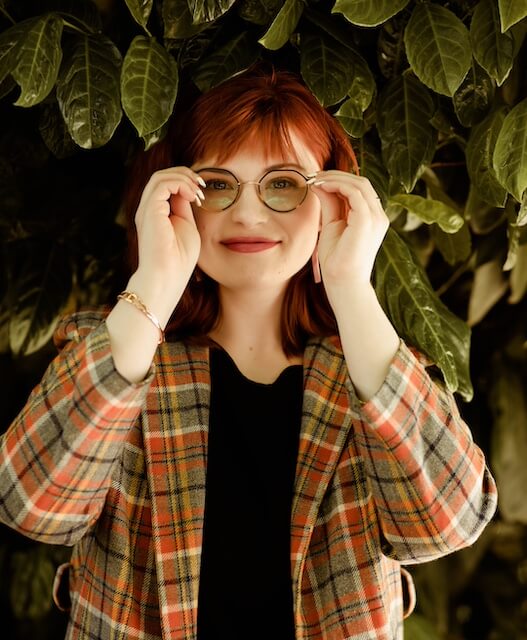 Headshot of Kat, a woman with medium-length red hair and glasses